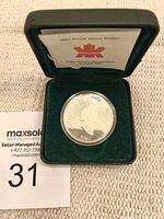 Front side of silver dollar coin showing Queen Elizabeth II in protective capsule inside green case