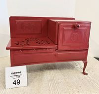 Front view of red child's electric stove with embossed details and decorative vent holes, showing condition and overall design.