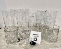 Front view of assorted clear glass barware including branded glasses and wine bubbler on a neutral fabric surface