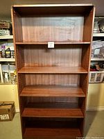 Front view of cherry veneer bookcase showing five shelves and adjustable shelf peg holes along the sides.