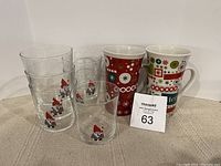 Photo showing 4 clear glasses with Santa Claus design and 2 ceramic mugs with Christmas patterns, displayed against a white background.