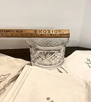 Crystal dish on a dark surface next to assorted linens, ruler showing approx 3.5 inch height and width