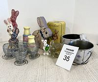 Front view of assorted Easter decor including ceramic bunnies, metal tins, glass bunny figurine, spiral egg cups, and candle holders.