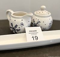 Set of winter themed creamer, sugar shaker, and olive dish displayed on dark counter with auction card