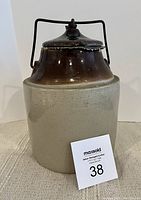 Front view of the large stoneware crock with lid and wire handle, showing overall shape and finish.