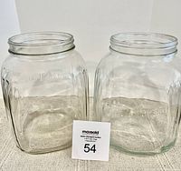 Two large square clear glass jars showing their shape and embossed volume markings on the side, placed side by side on a surface with a lot number card.