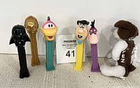 Six assorted PEZ dispensers shown in a row including Darth Vader, C-3PO gold, yellow bird, Fred Flintstone, purple chicken, and plush dog.