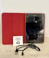 Samsung Galaxy Tab A tablet in a red protective case with a USB charging cable placed in front, displayed upright.