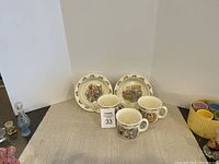 Five-piece set of vintage Royal Doulton Bunnykins bone china dishware consisting of three illustrated mugs and two matching small plates with bunny scene decorations.