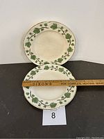 Two Sovereign Potters vintage luncheon plates displayed flat with visible green ivy leaf border pattern and gold trim. Plates measure about 9 inches wide as shown by ruler.