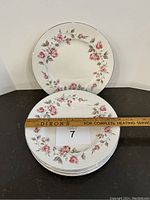 Top view of six stacked plates showing floral pink rose design and ruler indicating plate diameter of approximately 7 inches