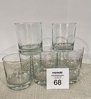 Eight clear heavy bottomed glasses arranged in two rows, with three glasses in front and two stacked on top, showing their cylindrical shape and thick bases.