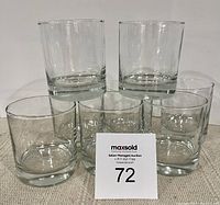 Eight heavy bottomed clear whiskey glasses photographed grouped together on a neutral surface.