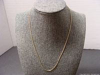 Full view of the 16 inch thin gold chain necklace displayed on a neutral fabric bust.