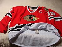 Red Chicago Blackhawks NHL jersey with large logo on front and Captain 'C' on shoulder.