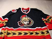 Front view of black NHL Ottawa Senators CCM jersey with large team logo and red, gold, black trim.