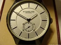 Close-up of the silver-tone dial showing black hour markers, black hour and minute hands, small seconds subdial, and Stuhrling Original logo.