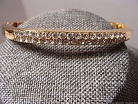 Close-up view of the Swarovski bangle front section showing two rows of clear rhinestones set into gold-tone metal.