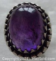 Close-up front view showing purple oval amethyst cabochon in sterling silver multi-prong setting with twisted and double circle border.