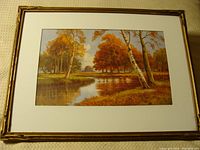 Full view of framed lithograph showing autumnal trees by a river.