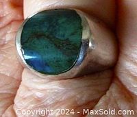 Close-up of ring top showing irregular oval green-blue Stone of Elat set in curved silver bezel on hand.