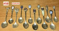 Photo showing 12 souvenir spoons arranged side by side on a wooden surface, highlighting their detailed handles and enamel crests.
