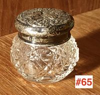 Full view of the antique crystal jar with ornate silver lid sitting on a wooden surface.