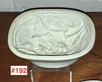 Top view of the antique blancmange mould showing detailed floral and leaf relief pattern in cream color with some aging signs.