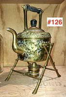 Full front view of the brass teapot on stand with visible floral embossing and integrated burner under the kettle