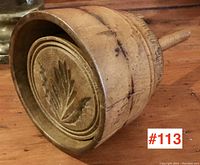 Side view of the wooden butter mould showing the carved leaf pattern on the circular base and handle attached