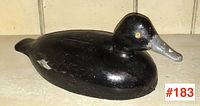 Side view of the black painted wooden duck decoy with grey bill and yellow eyes showing minor paint wear.
