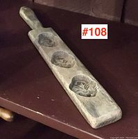 Side view of the wooden sugar mould paddle showing handle and three floral cavities