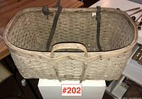 Front view of the antique split ash basket showing shape, weave pattern, and leather straps