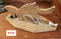 Front angle showing the carved wooden animal shape and wooden base with operating string.