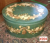 Large oval toleware box painted teal with floral garlands and ribbon design on the top.