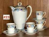 Coffee pot and four coffee cups with saucers displayed together on a shelf, showing overall set and decorative pattern clearly.