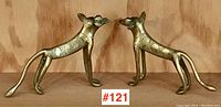 Frontal and side view showing paired brass figures of African wild dogs standing facing each other on wooden shelf.