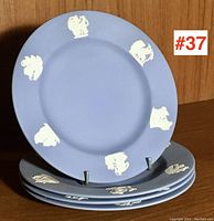 Set of 4 Wedgwood jasperware style blue plates with white classical reliefs, one displayed upright and others stacked.