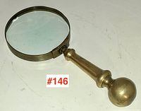 Side view of Victorian brass magnifying glass showing the brass handle and circular glass lens with slight chip.
