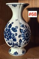 Front view of the vintage Delft vase showing full floral design and overall shape, positioned upright on wood shelf.