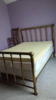 Full side view of the brass bed with memory foam topper and boxspring, showing the worn brass finish and mattress layers.