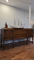Front view of antique wooden buffet showing two drawers in center and two cupboards with carved doors at sides, turned legs and cross braces, wooden top with wear.