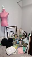 Full view of lot contents including dress form, yarn balls, picture frames, linen rolls, and small craft items clustered on floor.