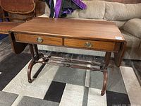 Full view of wooden drop leaf table showing top, two drawers, side leaves and legs with stretchers.