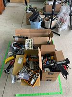 Overall view of multiple boxes with assorted hardware and tools including rivet tools, wire spools, and wrenches arranged on garage floor.