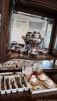 Photo of vintage silver coffee percolator and matching cream and sugar bowls in a wooden cabinet mirror reflection.