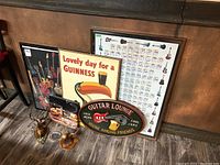Overall view of the lot showing the guitar chord poster, Guinness toucan plaque, Guitar Lounge plaque, elk and moose carvings, and ashtray on floor against wall.