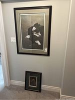 Both framed prints hanging and resting on the floor against a wall showing sizes and framing style.