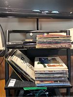 Photo showing a stack of LP records, two 45 singles, and CDs on a shelving unit.