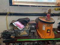 Triton spindle sander with sanding sleeves and plastic tote with sanding sleeves and accessories on workbench.